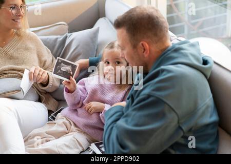 Tochter zeigt dem Vater zu Hause Ultraschallfoto Stockfoto