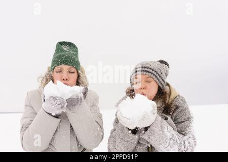 Freunde tragen Strickmützen, die im Winter Schnee blasen Stockfoto