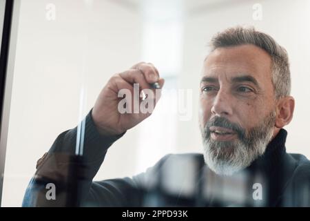 Reifer Geschäftsmann, der mit Filzstift auf Glas schreibt Stockfoto