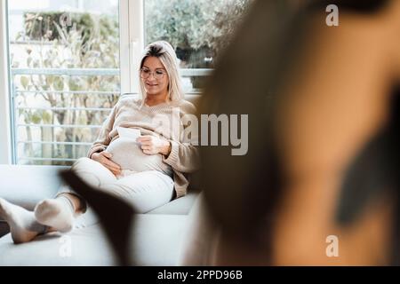 Lächelnde Frau, die zu Hause Ultraschallfotos ansieht Stockfoto