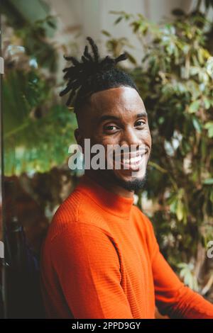 Glücklicher junger Mann, der neben der Pflanze sitzt Stockfoto