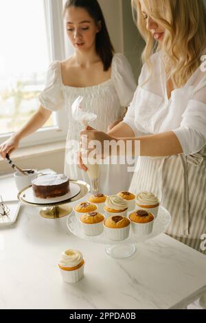 Eine Frau mit einer Freundin, die zu Hause Kuchen zubereitet und Cupcakes dekoriert Stockfoto