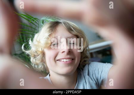 Glücklicher blonder Junge, der durch den Fingerrahmen schaut Stockfoto