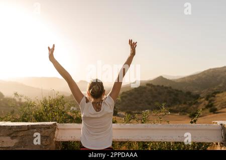 Sorglose Frau mit erhobenen Armen, die den Sonnenuntergang genießt Stockfoto