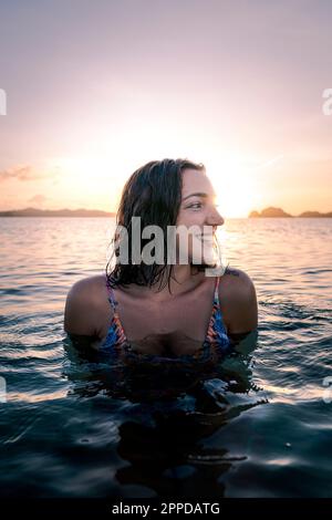 Lächelnde junge Frau, die sich bei Sonnenuntergang im Wasser amüsiert Stockfoto