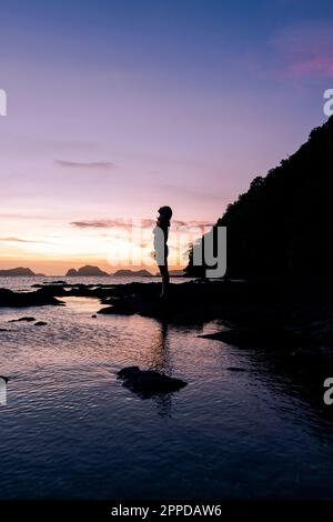 Silhouette einer Frau, die auf einem Felsen am Strand steht Stockfoto