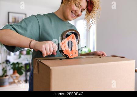 Lächelnde junge Frau, die eine Kiste mit Klebeband verpackt hat Stockfoto