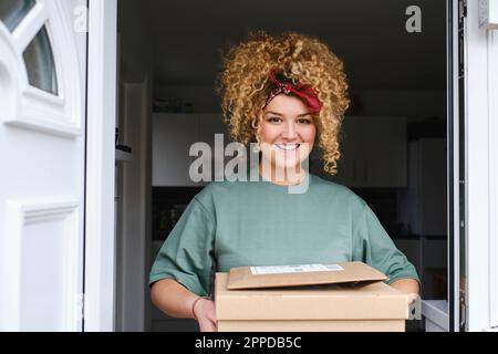 Glückliche junge Frau mit Paketen, die vor der Tür stehen Stockfoto