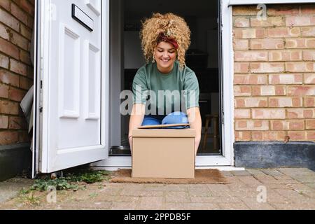 Glückliche junge Frau, die Pakete von der Tür abholt Stockfoto