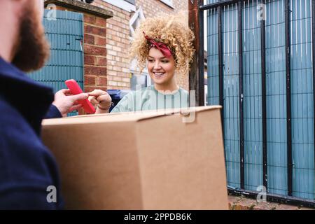 Lächelnde junge Frau, die ein Smartphone berührt, das von einem Lieferenden gehalten wird Stockfoto