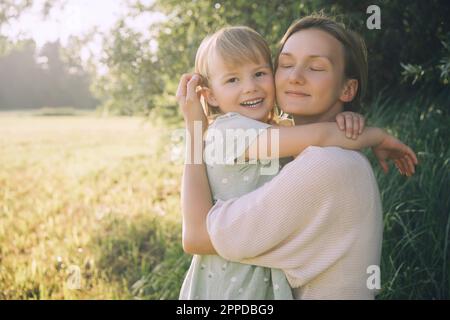 Lächelnde Mutter umarmte Tochter an einem sonnigen Tag in der Natur Stockfoto