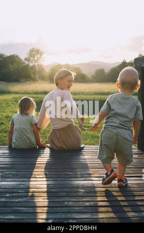 Mutter sitzt mit Tochter und Sohn auf einer hölzernen Fußgängerbrücke Stockfoto