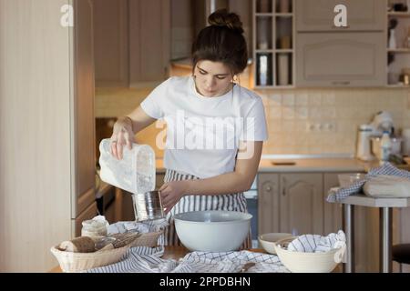 Junge Frau, die Mehl in den Messbecher gießt Stockfoto