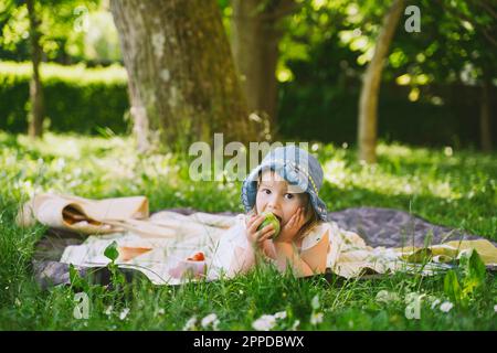 Mädchen, die grünen Apfel essen und im Garten auf Gras liegen Stockfoto