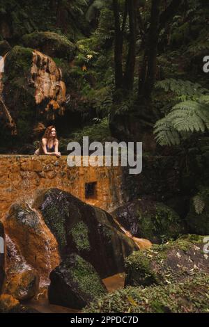 Junge Frau, die sich im Wald an die Wand lehnt Stockfoto