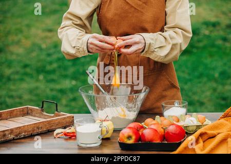 Frau, die ein Ei in einer Mischschüssel am Tisch im Garten zerbricht Stockfoto