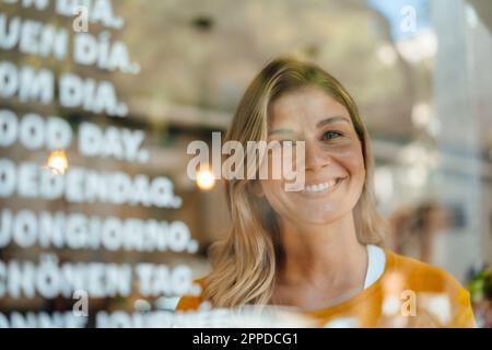 Glückliche Frau mit blonden Haaren im Café, durch Glas gesehen Stockfoto