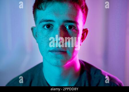Trauriger junger Mann mit beleuchtetem Neonlicht im Gesicht Stockfoto