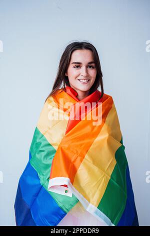 Glückliche junge Frau mit Regenbogenfahne vor der Wand Stockfoto