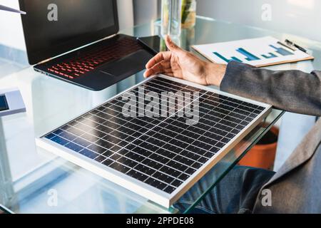 Geschäftsmann mit Sonnenkollektor am Schreibtisch im Heimbüro Stockfoto