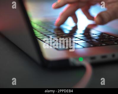 Hände, die im Home Office im Dunkeln auf der beleuchteten Laptop-Tastatur tippen Stockfoto