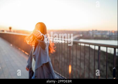 Eine Frau, die auf der Brücke steht und bei Sonnenuntergang ihre Hand ausstreckt Stockfoto