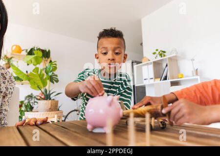 Der Junge steckt die Münze zu Hause in die Sparschweinbank Stockfoto