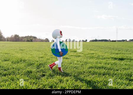 Ein Mädchen, das als Astronautin verkleidet ist und auf dem Gras die Erde ausgeschnitten hat Stockfoto