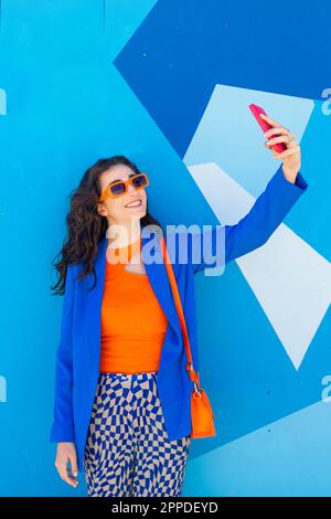 Glückliche Frau mit Sonnenbrille, die Selfie vor der blauen Wand macht Stockfoto