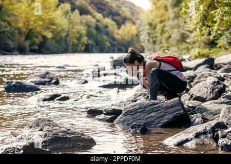 Durstige Frau, die Wasser aus dem Fluss trinkt Stockfoto