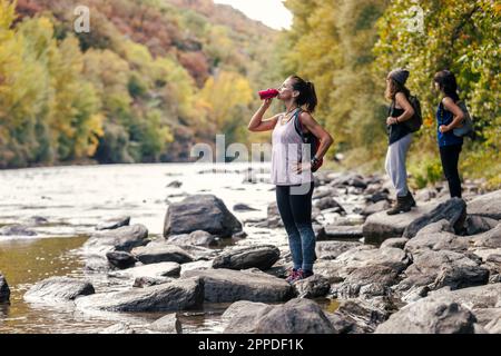 Frau trinkt Wasser aus einer Flasche mit im Hintergrund stehenden Töchtern Stockfoto