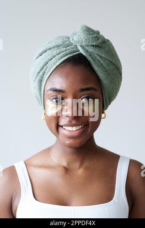 Lächelnde Frau mit Handtuch auf dem Kopf vor der Wand Stockfoto