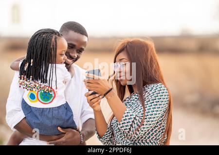 Lächelnde Frau, die Mann und Tochter ein Smartphone zeigt Stockfoto