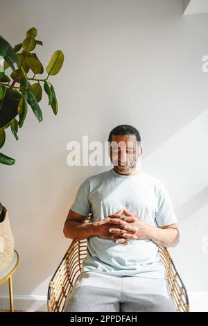 Lächelnder reifer Mann mit gefalteten Händen, der auf dem Stuhl sitzt Stockfoto