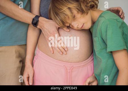 Muttertag, Vatertag, kleiner süßer blonder Junge, der moms schwangeren Bauch berührt, Ehemann, der seine Frau am Bauch hält Stockfoto