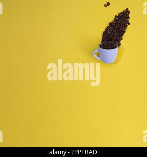 Kaffeebohnen aus einer weißen Tasse auf gelbem Hintergrund mit Kopierbereich. Minimale flache Laienzusammensetzung. Stockfoto