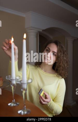 Ein junges Mädchen mit langen Haaren leuchtet Kerzen in der Küche zu Hause. Stockfoto