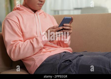 Ein seriöser junger Mann, der zu Hause auf der Couch sitzt und Freunden SMS schreibt Stockfoto