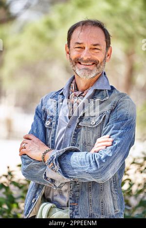 Selbstbewusster Mann, der mit gekreuzten Armen posiert und für die Kamera lächelt Stockfoto