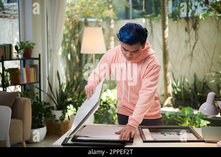 Kreativer junger Mann, der schwarz-weiß gedruckte Fotos in Rahmen legt Stockfoto