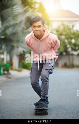 Junger Mann mit blauen Haaren, der auf der Straße Skateboard fährt Stockfoto