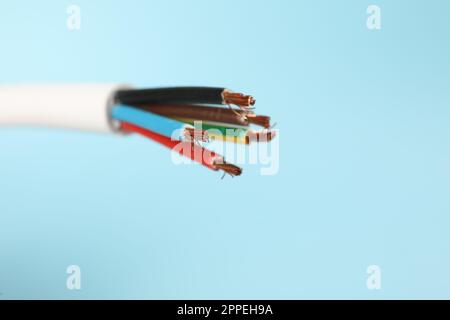 Kabel mit abisolierten elektrischen Drähten auf hellblauem Hintergrund, Nahaufnahme Stockfoto