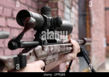 Ein Soldat hält ein modernes, leistungsstarkes Scharfschützengewehr mit teleskopischer Sicht draußen, Nahaufnahme Stockfoto