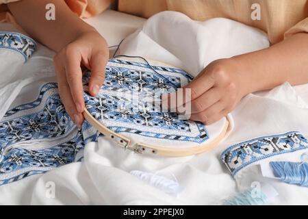 Besticktes Frauenhemd mit blauem Faden am Tisch, Nahaufnahme. Ukrainische Nationalkleidung Stockfoto