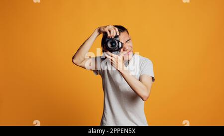 Junger professioneller Fotograf, der mit dslr-Kamera Fotos macht und Spaß mit Fotos hat, während er im Studio fotografiert. Männliches Model posiert mit Ausrüstung, fühlt sich selbstsicher. Stockfoto