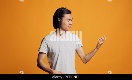 Moderne Person spielt Luftgitarre, hört Musik, hat Spaß mit dem Audio-Headset im Studio. Das junge Model fühlt sich fröhlich und cool mit den Kopfhörern, singt ein mp3-Lied und lächelt. Stockfoto