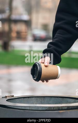 Ein Mann wirft einen Papierbecher in den Mülleimer im Park. Stockfoto