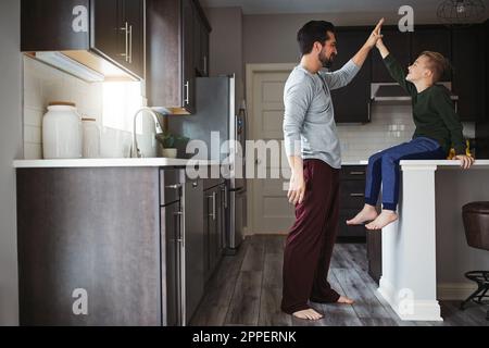 Gut gemacht. Die volle Länge eines gutaussehenden jungen Mannes und seines Sohnes, der High Five in der Küche macht. Stockfoto