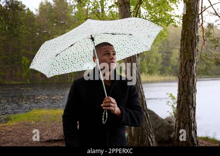 Ein junger Mann hält einen Schirm am See Stockfoto