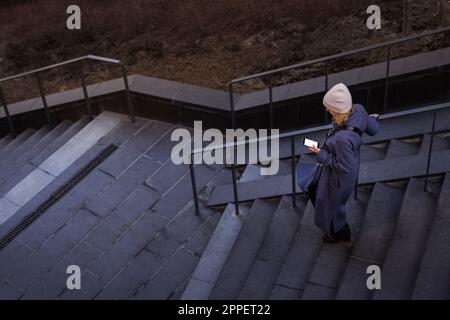 Junge Frau, die die Treppe runtergeht und telefoniert Stockfoto